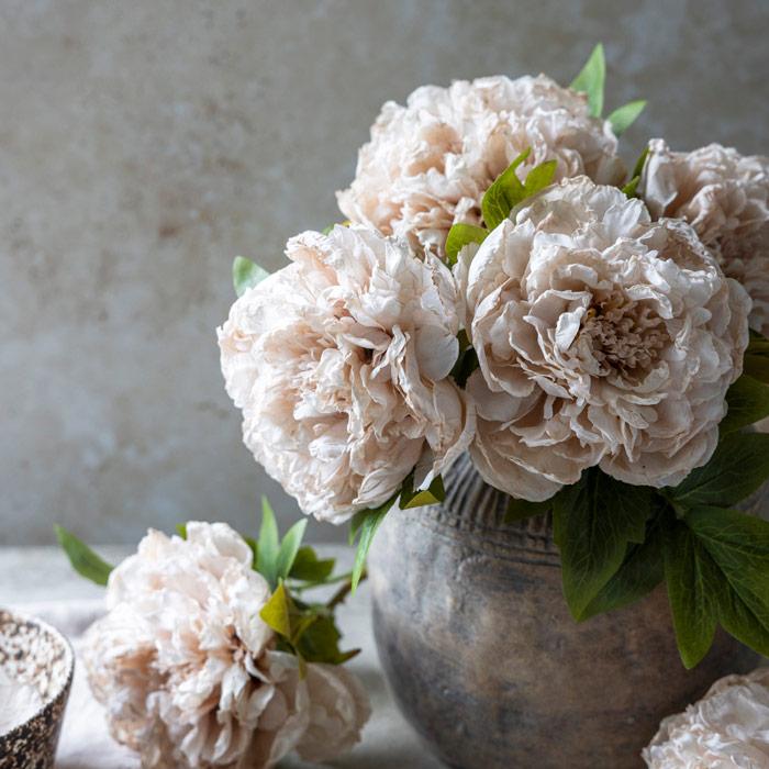 Bouquet of light pink flowers in a textured vase on a neutral background