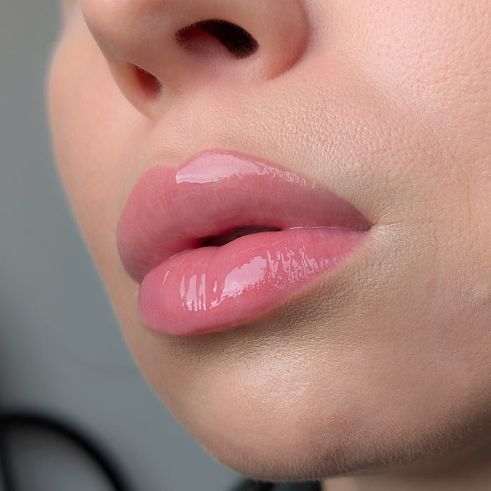 Close-up of a person's lips with pink lip gloss Lipss Rose on a blurred background