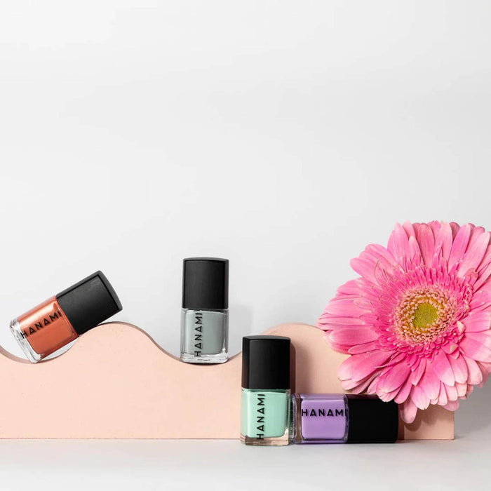 Four nail polish bottles with black caps and colorful labels next to a pink flower on a white background.