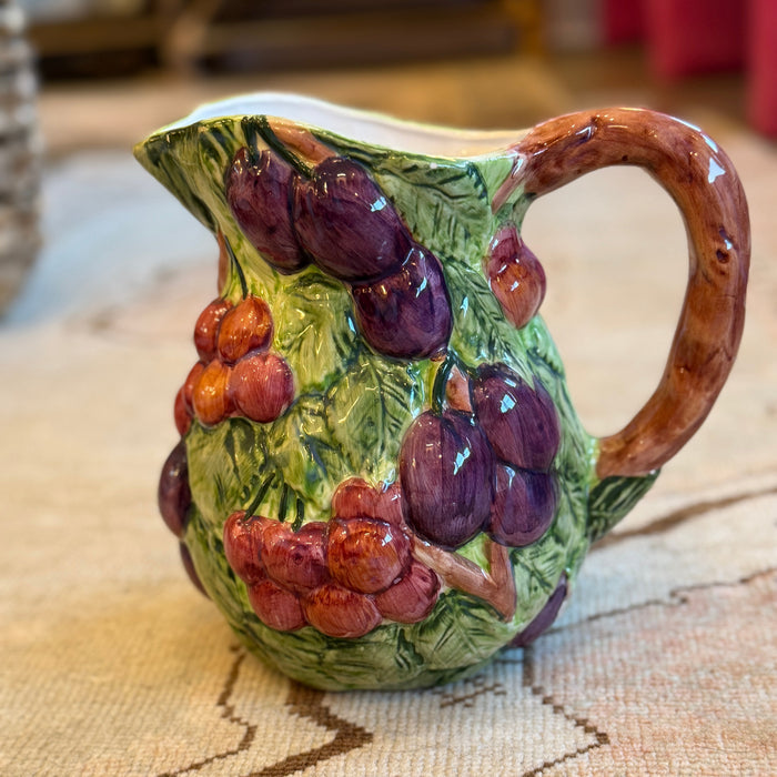 Ceramic pitcher with grape design on a textured surface