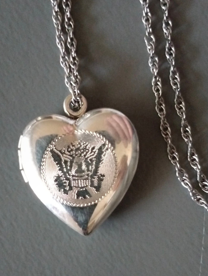 Silver heart-shaped locket with intricate design on a chain against a dark background