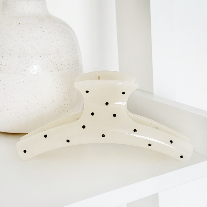 White polka dot claw clip on a white shelf next to a speckled white vase.
