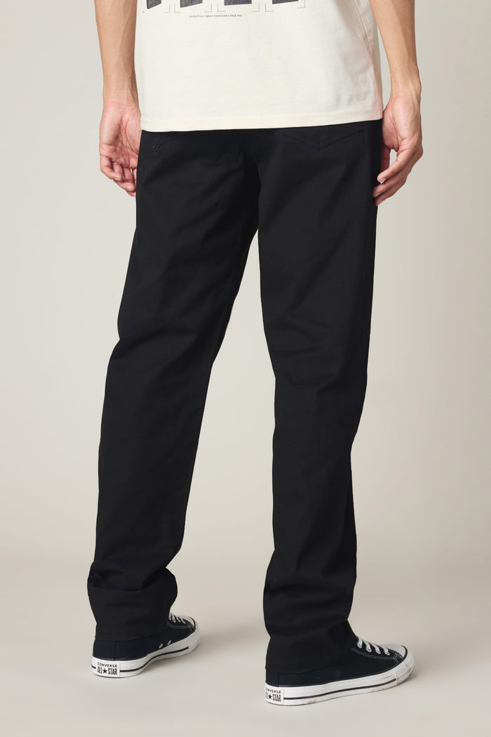 A person stands facing away against a plain background, wearing a white shirt, black-and-white sneakers, and 686 Men's Everywhere® Standard Pant - Relaxed Fit from 686 in black.