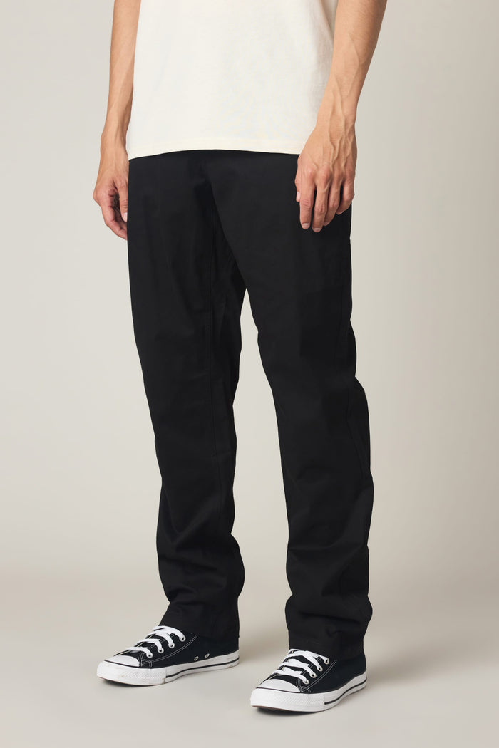 A person is seen from the waist down, standing against a plain background, wearing 686 Men's Everywhere® Standard Pant - Relaxed Fit in black.