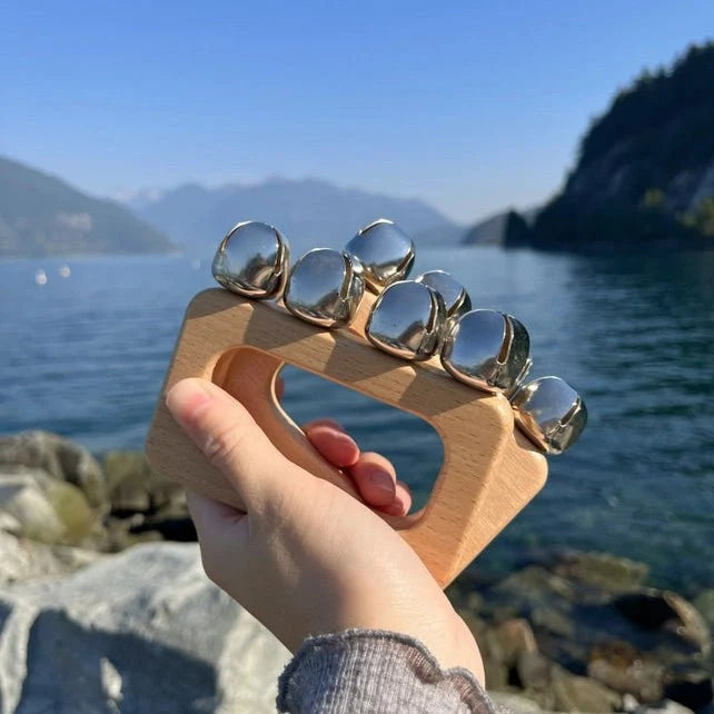 Hand holding a wooden tool with metal weights against a scenic background of water and mountains.