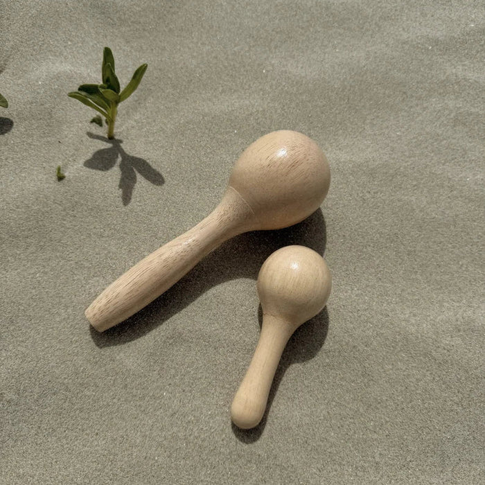One large and one small wooden maraca on sandy ground with a small plant in the background