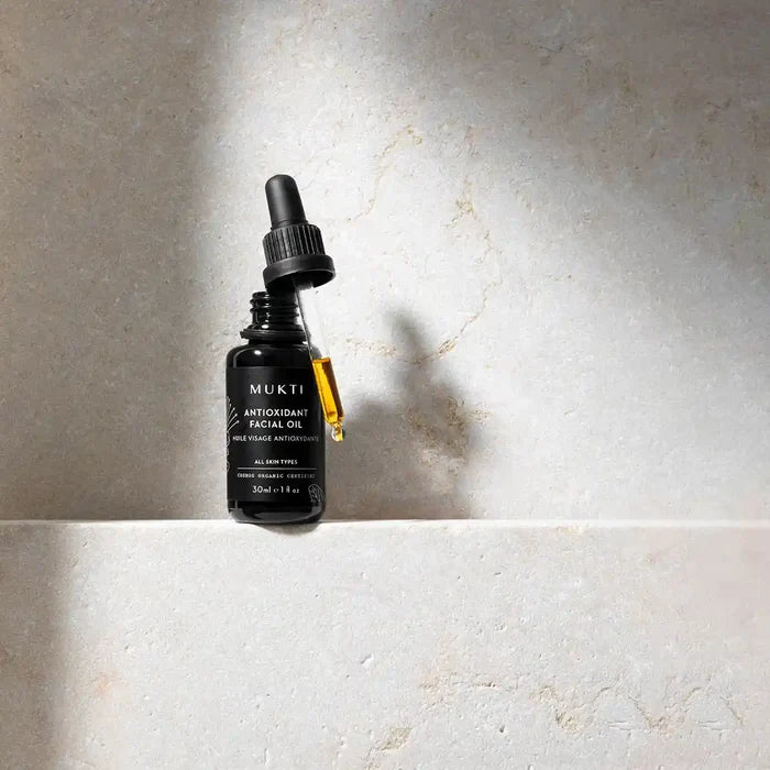 MUKTI Antioxidant Facial Oil on a marbled stone surface with lid off showing dropper filled with oil.