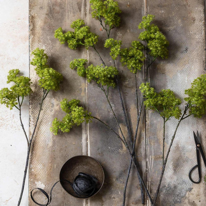 Green floral branches on a textured surface with a pair of scissors.