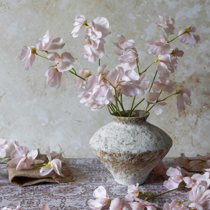 Pink flowers in a textured vase on a lace tablecloth with a floral background