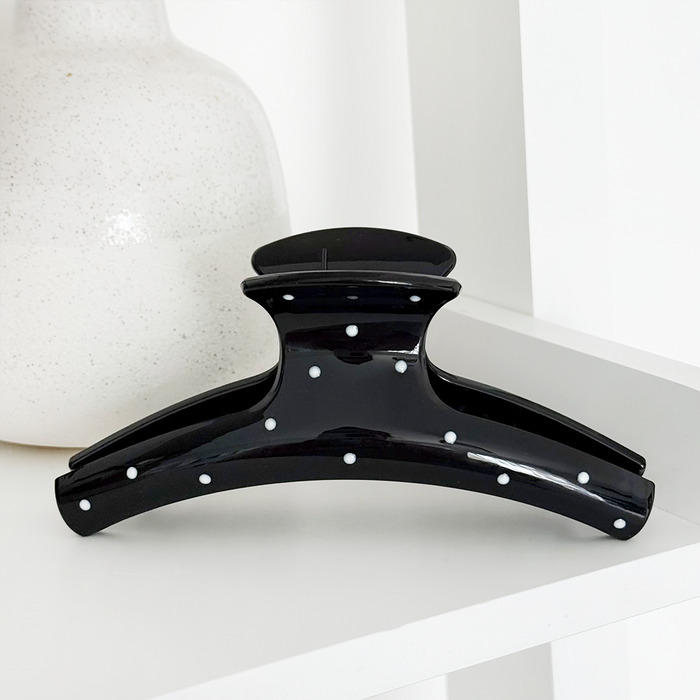 Black polka dot claw clip by Coconut Lane on a white shelf beside a speckled vase.