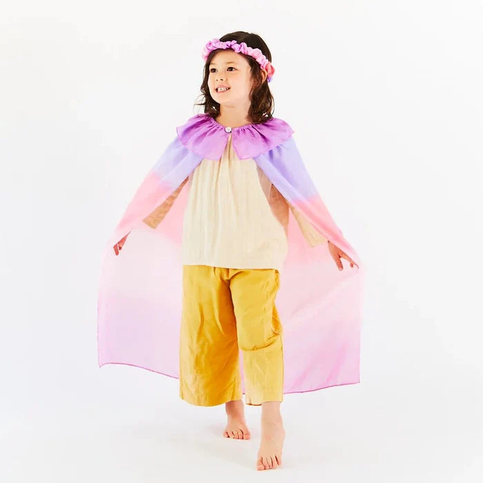 Child wearing a colorful pink and purple cape and yellow pants on a white background