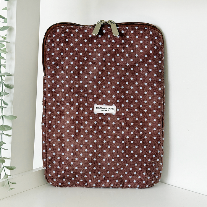 Brown and blue polka dot iPad sleeve by Coconut Lane standing upright on a shelf next to a leafy green plant.
