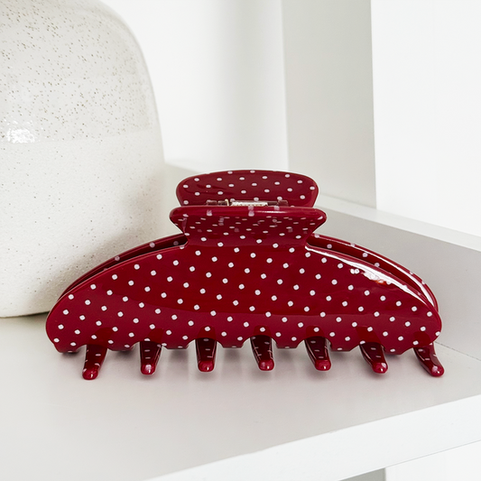 Burgundy claw clip with white polka dots, displayed next to a ceramic vase on a shelf.