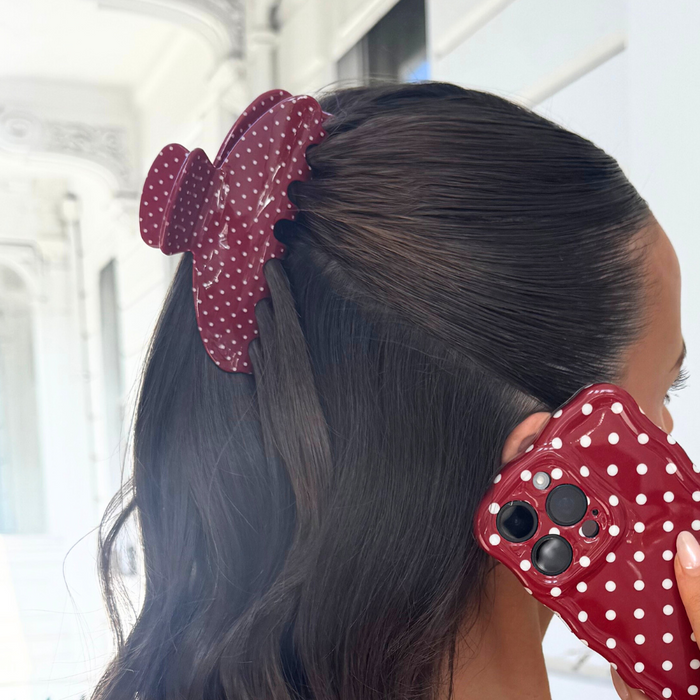 Woman with dark hair wears a burgundy polka dot claw clip and holds a matching phone case.