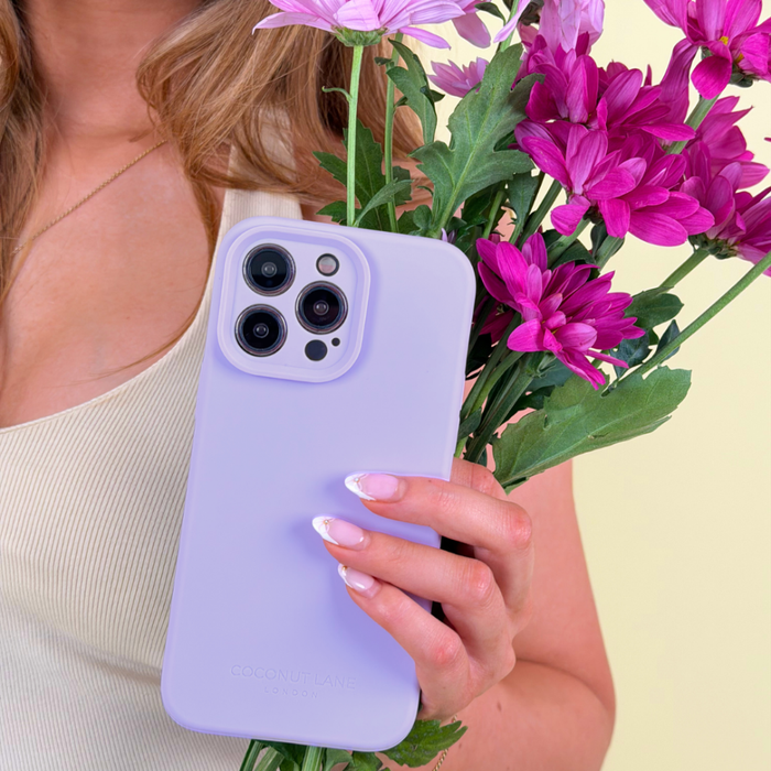 Woman with matching nails holds purple flowers and a lilac Coconut Lane soft silicone phone case.