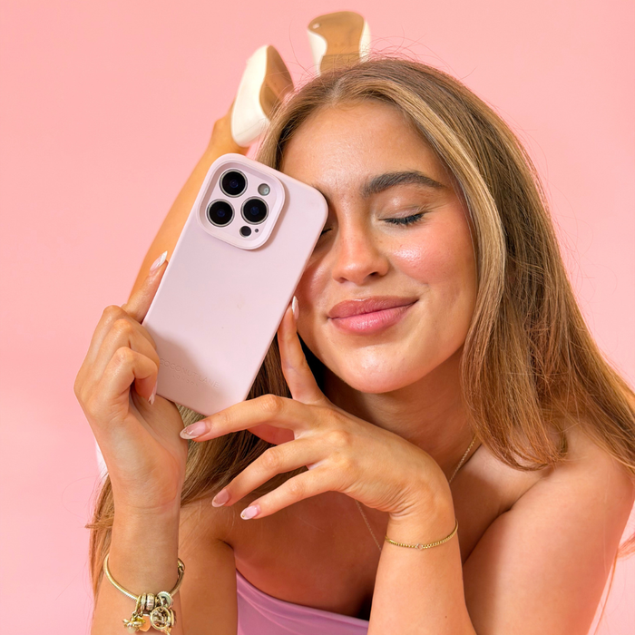 Girl smiling in studio shoot pink background holding butter soft pink phone case