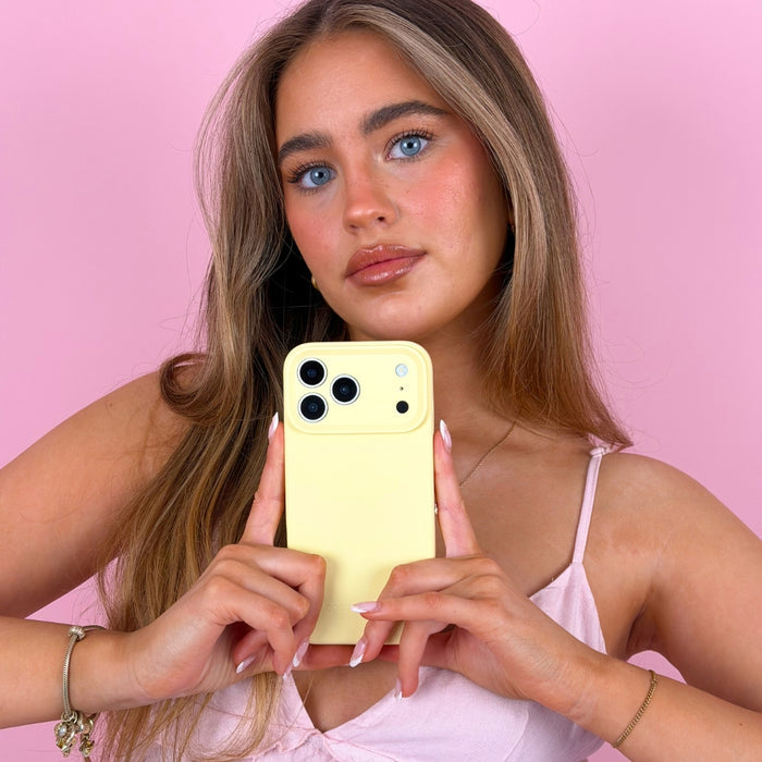 Woman in a pink top holds a yellow Butter Soft Silicone Phone Case by Coconut Lane against a pink background.