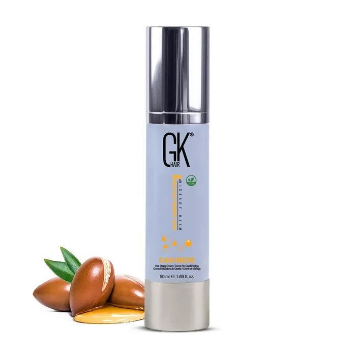GK Hair Cashmere Hair Cream, tall pale blue 50 ml bottle with a silver pump and vegan badge, beside cracked argan nuts