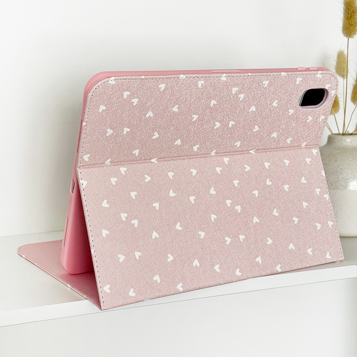 Coconut Lane iPad case with white heart pattern, open on a shelf beside a beige vase of dried flowers.
