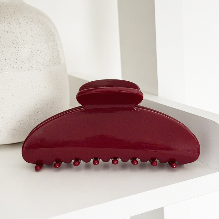 Cherry red Coconut Lane claw clip on a white shelf next to a ceramic vase.