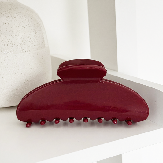 Cherry red Coconut Lane claw clip on a white shelf next to a ceramic vase.