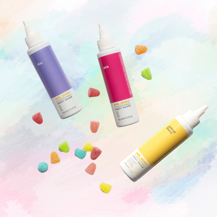 Three colorful bottles of milk_shake direct colour with sprayer nozzles on a pastel background with candy-like shapes.
