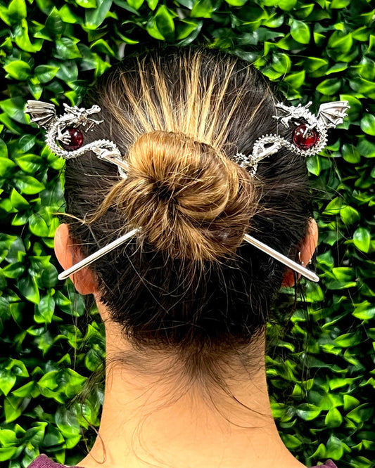 Model wearing silver Dragon Hair Sticks with 3D dragons holding red crystal spheres in a bun hairstyle, back view.