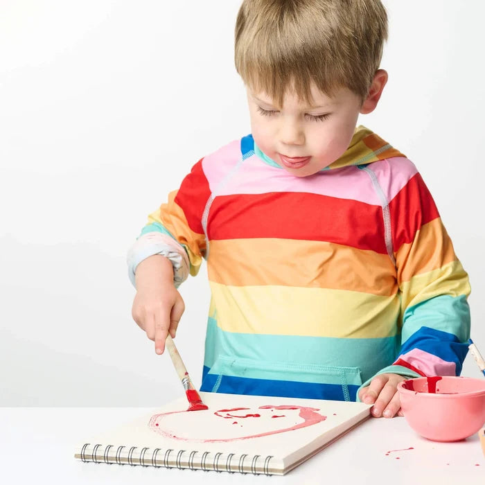 Child in a colorful striped shirt painting on a white surface