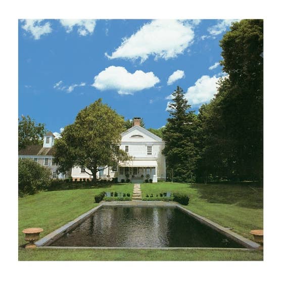 Large white house with a pond in a lush green garden under a blue sky.