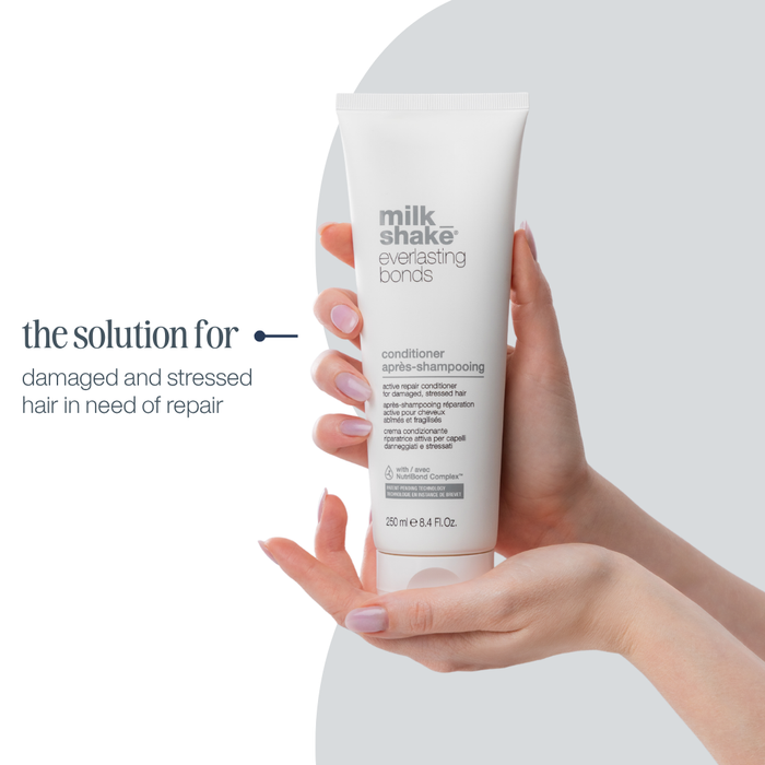 Hand holding a tube of 'milk_shake' conditioner with text about hair care on a white background