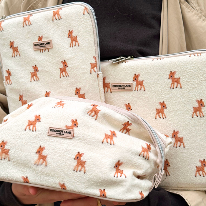 Three cream iPad sleeves with brown deer prints and zippers, held by someone in a tan jacket.