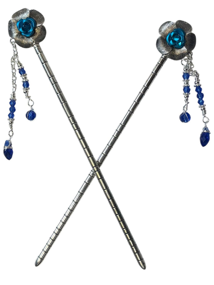 Pair of silver flower hair sticks with blue rose centers and blue crystal bead dangle chains, shown crossed on a white background to display the front view.