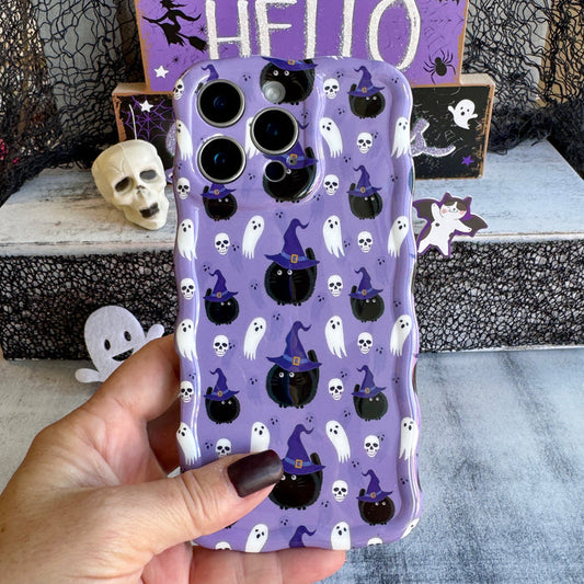 Ghostly Whisker's Wavy Luxe MagSafe iPhone case held in hand, lavender with black witch-hat cats, white ghosts and mini skulls.
