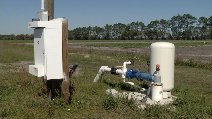 Irrigation system pump with pressure tank and control panel installed in a grassy agricultural field with trees behind