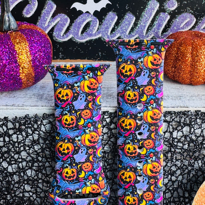 Both halves of the Jack-O-Lantern Jive Apple Watch band standing upright between orange and purple glitter pumpkins.