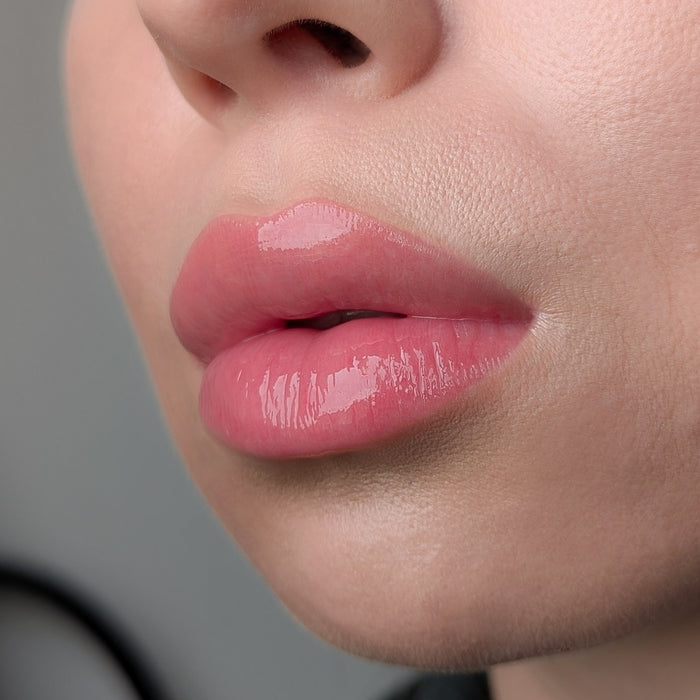 Close-up of a person's lips with pink lip gloss Lipss Butter Croissant on a neutral background