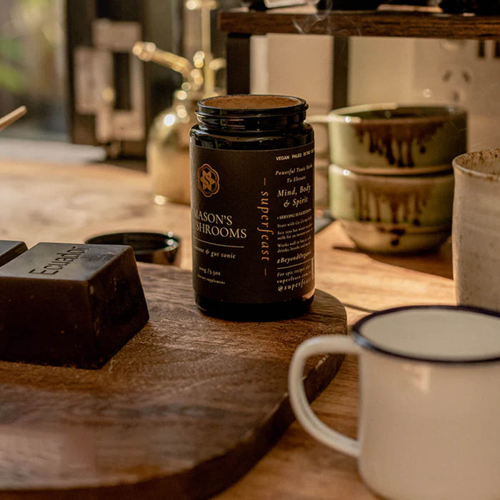 Bottle of 'Mason's Mushrooms' on a wooden surface with a mug and chocolate bars in the background.