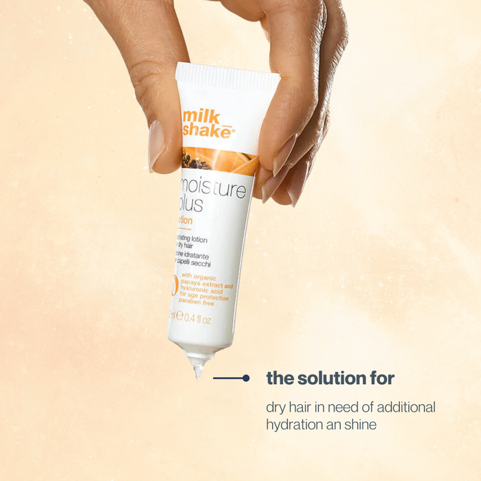 Hand holding a tube of milk_shake hair lotion against a beige background