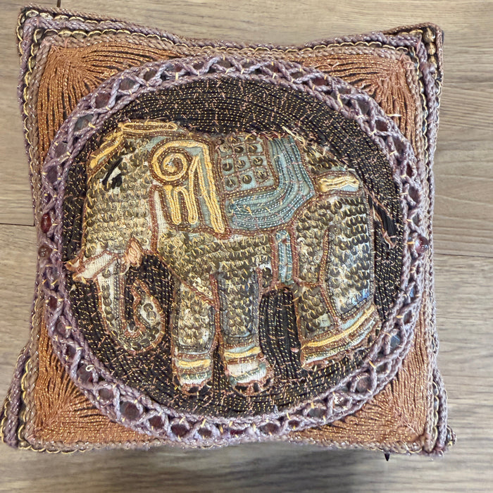 Decorative pillow with embroidered elephant design on a wooden surface