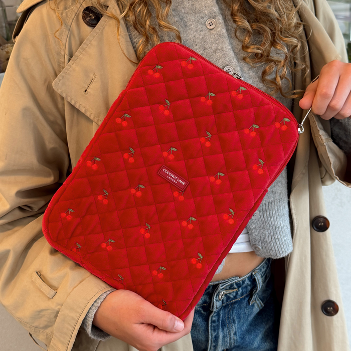 Quilted cherry red velvet iPad sleeve by Coconut Lane held by person in a beige trench coat, grey sweater, and jeans.