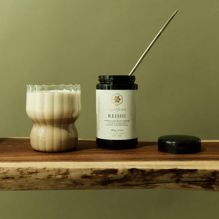 Jar of Reishi mushroom supplement with a candle and incense stick on a wooden surface against a green background