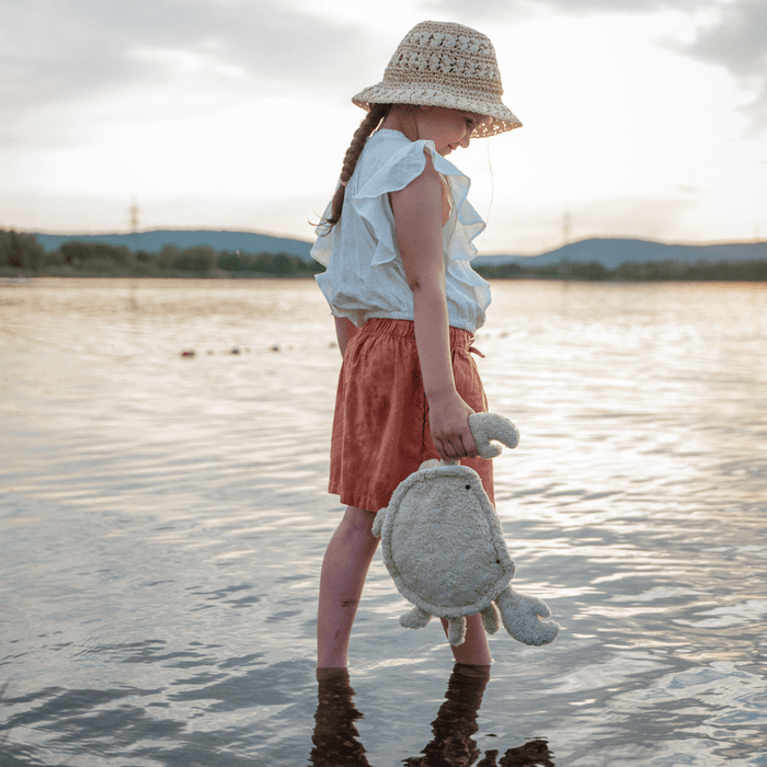 Young girl holding a plush crab by a lake with a cloudy sky.