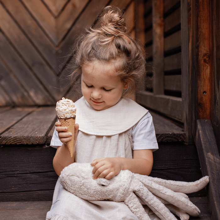 Child holding a ice cream cone and plush toy against a wooden background