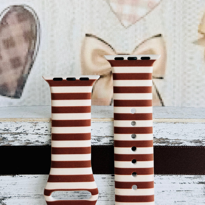 Sweet Espresso Stripes Apple Watch band front view of both strap halves against a cream knit and bow backdrop, showing the brown stripe repeat and adjustment pin holes.