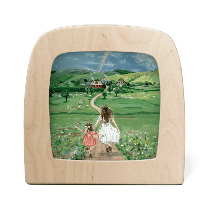 Wooden frame with a painted scene of two girls in a field with a rainbow in the background