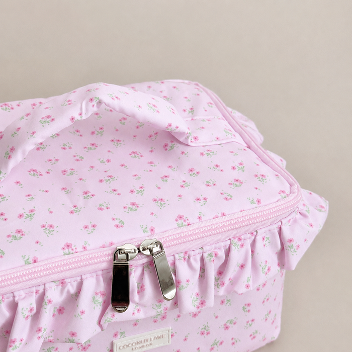 Pink floral patterned Vanity Bag with ruffled trim, handle and zip closure.