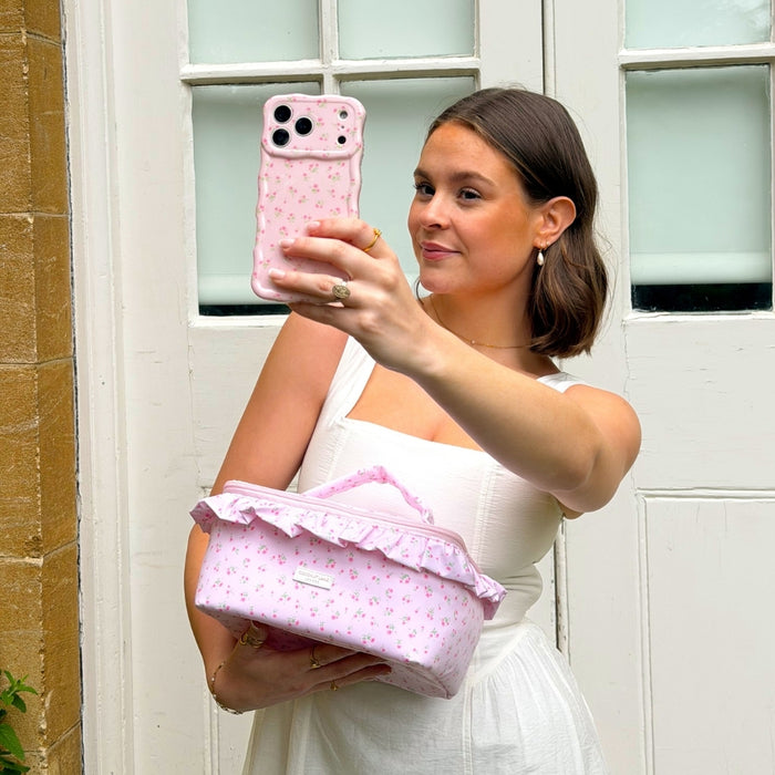 Woman holding a ditsy floral pink phone case and matching vanity case in front of a white door.