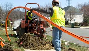 Two construction workers operating underground utility installation equipment on a residential street during daytime