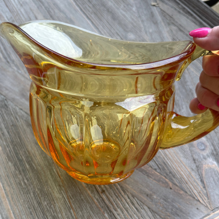 Yellow glass pitcher held by a hand on a wooden surface