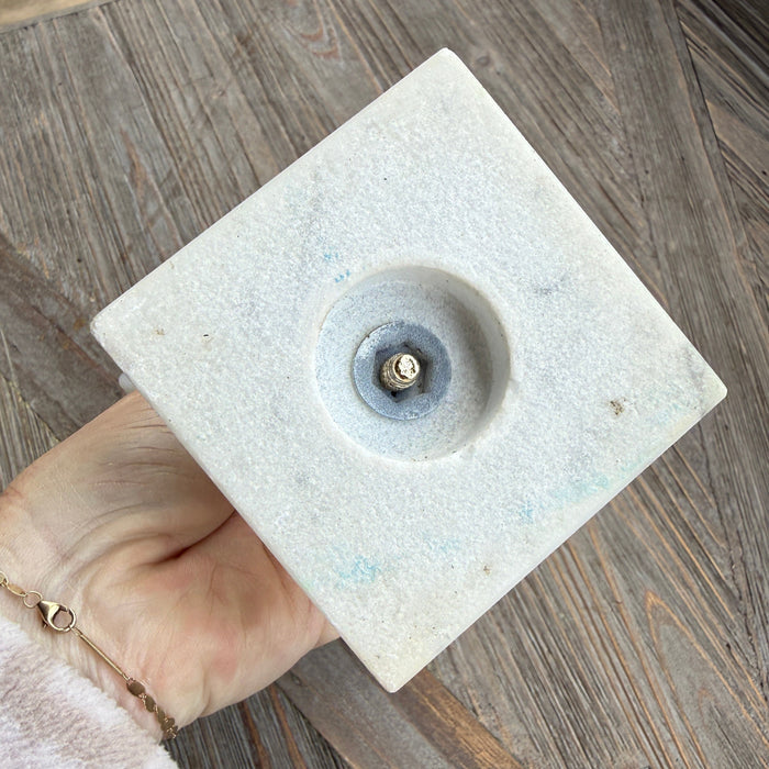 Square stone object with central hole held by a hand on a wooden surface